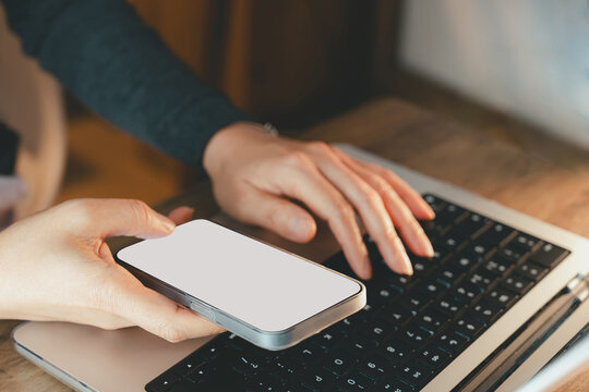 Business woman hands using smartphone and typing on laptop keyboard, showcasing digital multitasking, online communication, mobile synchronization, and modern technology in workplace or home office.