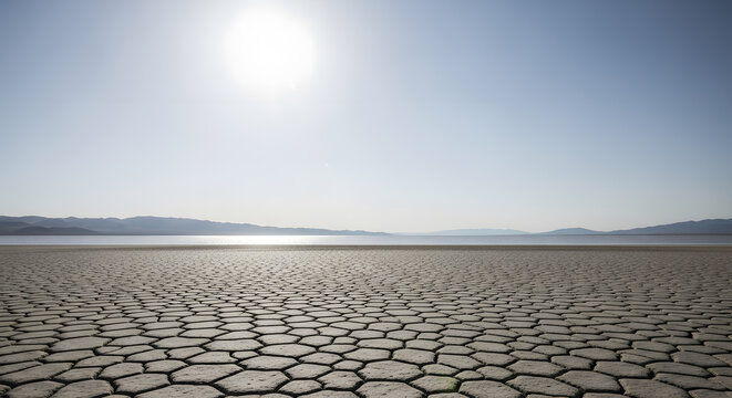 Cracked earth on a dry lake bed under a vast sky with distant mountains and sun