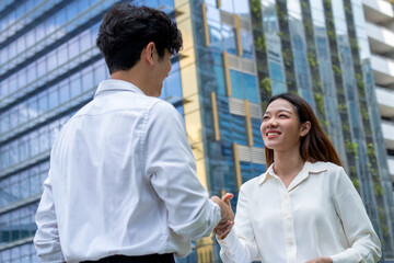 Asian businessman and businesswoman making handshake outdoors in city. 