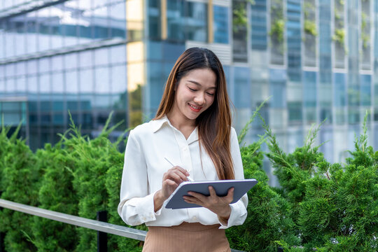 Asian young businesswoman using digital tablet while standing in the city. - Powered by Adobe