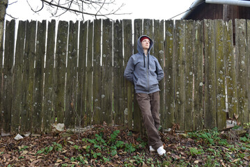 Young woman in grey hoodie leaning on rustic fence