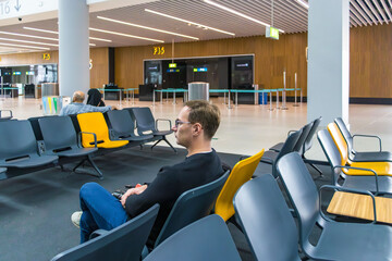 Man sitting in airport waiting area with luggage and backpack, waiting for flight, modern terminal interior