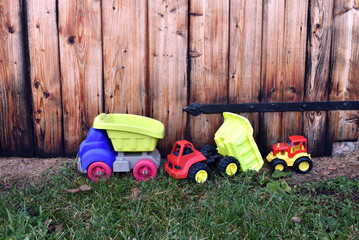 Colorful plastic toy trucks on grass against vintage wooden background