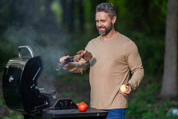 Man with barbeque roast meat outdoor. Grilling and barbecue. BBQ and grill. Hispanic man preparing...