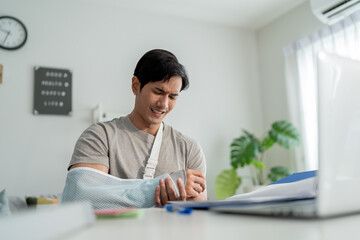Injured Asian businessman wearing hand splint while working from home.
