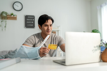 Injured Asian man with hand splint using laptop for online shopping. 