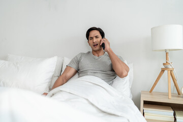 Asian depressed young man talking on mobile phone in bedroom at home. 