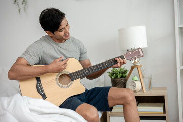 Asian handsome man musician playing an acoustic guitar in house.