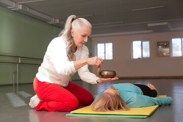 Senior woman doing massage therapy singing bowls in the gym. Sound therapy, recreation, meditation.