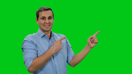 Young handsome man in light colored shirt smiling and pointing his fingers at something on green background