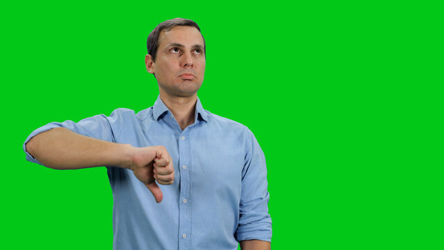 Thumb down sign gesture by young adult man expressing discontent disapproval dislike and disgust on green screen
