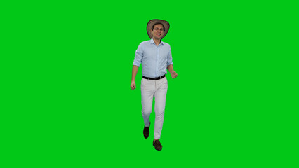 Carefree young happy businessman walking in light-colored shirt and pants with cowboy hat against green background