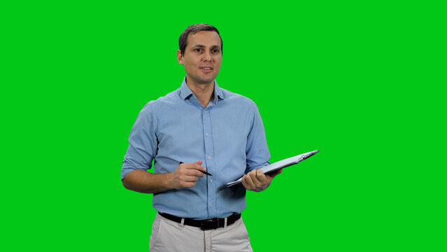 Handsome young businessman wearing light-blue shirt taking notes on clipboard against green background