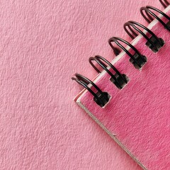 A detailed close up shot showcases a pink spiral bound notebook resting on a textured pink surface, with soft natural light highlighting the textures.