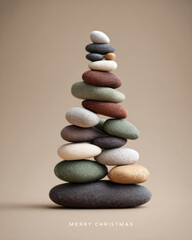 A tower of smooth, colorful stones stacked to form a Christmas tree shape on a light brown background with 'MERRY CHRISTMAS' text at the bottom.