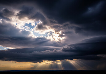 Spectacular sunlight breaking through a dramatic, textured sky filled with tumultuous storm clouds, casting luminous, detailed rays of light across the expansive horizon