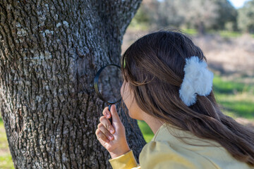 Young girl discovering nature using a magnifying glass on tree bark, learning about the environment and fostering curiosity during an outdoor educational activity