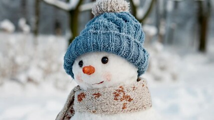 Adorable snowman with blue knitted hat and scarf stands in snowy winter park creating cozy festive Christmas greeting scene filled with childhood nostalgia