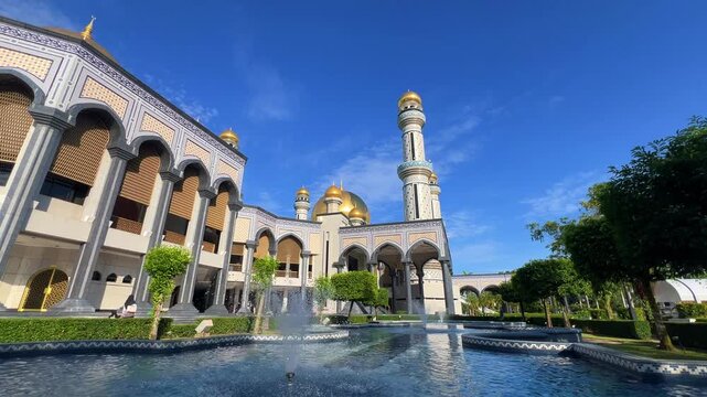 The golden dome and building of the Jamil Asra Hassan Al-Bolkiah Mosque in Bandar Seri Bagawan, Brunei Darussalam, are framed by tropical palm trees on a sunny day. Asia. 4К
