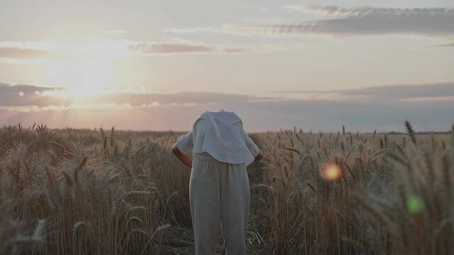Woman standing in golden wheat field at sunset, raising hands, bending down, and spreading arms for a moment of peace and freedom