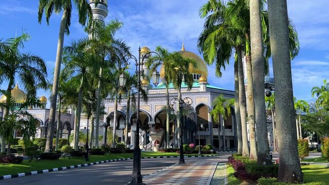 The golden dome and building of the Jamil Asra Hassan Al-Bolkiah Mosque in Bandar Seri Bagawan, Brunei Darussalam, are framed by tropical palm trees on a sunny day. Asia. 4К