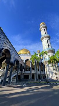 The golden dome and building of the Jamil Asra Hassan Al-Bolkiah Mosque in Bandar Seri Bagawan, Brunei Darussalam, are framed by tropical palm trees on a sunny day. Asia. 4К