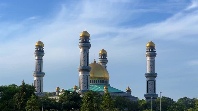 The golden dome and building of the Jamil Asra Hassan Al-Bolkiah Mosque in Bandar Seri Bagawan, Brunei Darussalam, are framed by tropical palm trees on a sunny day. Asia. 4К