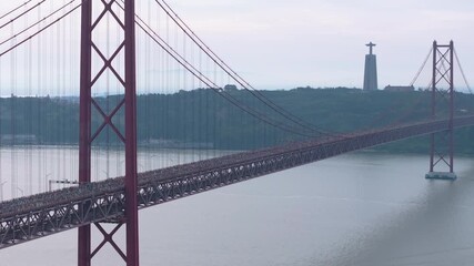 Cinematic aerial drone shot of thousands of long-distance runners crossing the iconic red 25th April suspension bridge in Lisbon, Portugal, with the Cristo Rei monument visible across the river