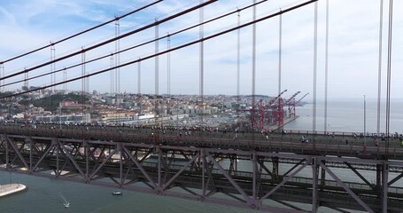 Half marathon and 10K long distance running event in Lisbon, Portugal, Europe. Runners crossing the iconic famous red 25th April suspension bridge. Slow panning aerial drone shot