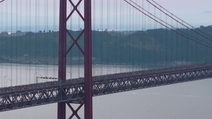 Half marathon and 10K long distance running event in Lisbon, Portugal, Europe. Runners crossing the iconic famous red 25th April suspension bridge. Cinematic sports aerial drone shot