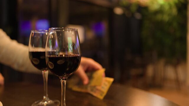 Hand Collects Lottery Tickets Beside Red Wine Glasses in Bar