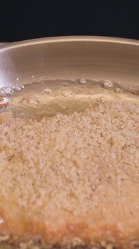 Close-up of breaded pork cutlet frying in hot oil in a stainless steel pan in a home kitchen, vertical format