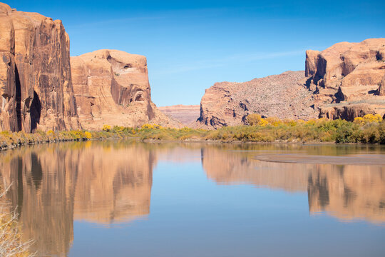 The main asphalt road runs through Arches National Park in eastern Utah, north of the city of Moab in the United States. It winds between rocks and trees colored yellow. Autumn time, sunny day.