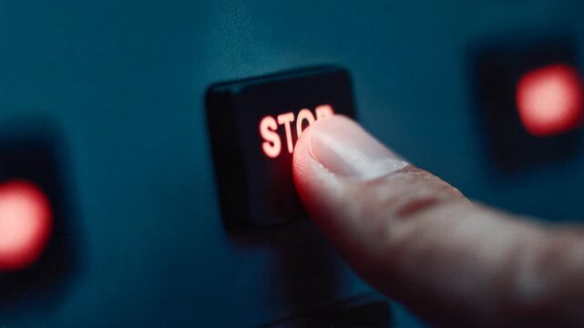 Finger firmly presses illuminated stop button on industrial control panel symbolizing emergency shutdown safety decision and critical risk management action