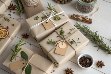 Natural eco holiday scene with kraft-wrapped gifts, herbs, dried oranges and spices on a white wooden surface. Sustainable Christmas aesthetic with warm neutral tones and clean seasonal styling.