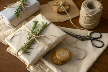 Warm rustic scene with kraft-wrapped gifts, twine, greenery and homemade cookies on a natural fabric surface. Eco-friendly holiday packaging with soft golden light and cozy handmade styling.