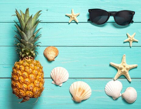 Tropical summer flat lay with pineapple, sunglasses, starfish, and seashells on a bright turquoise wooden background.