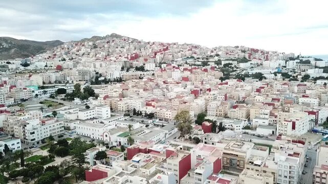Drone footage capturing the urban sprawl of Al Hoceima city adapting to the rugged topography of the Rif Mountain slopes in Northern Morocco.