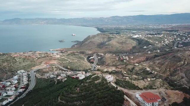 Drone footage showing white hillside homes in Al Hoceima. Scenic view of the Rif Mountains meeting the blue Mediterranean Sea coast in Morocco.