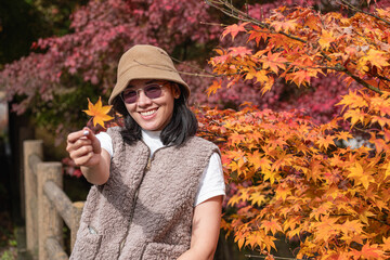 Woman holding autumn leaf outdoors near colorful fall foliage in park