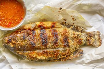 Grilled whole tilapia fish with salt crust served with spicy dipping sauce on paper.