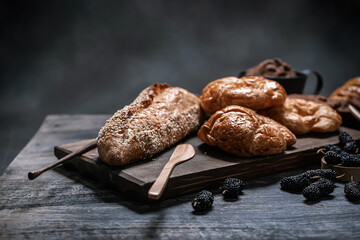 Fresh baked croissants and sesame baguette served on wooden board with fresh mulberries.
