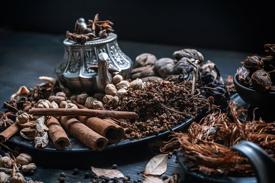 Assorted dried herbs and spices including cinnamon and star anise on dark wooden table.