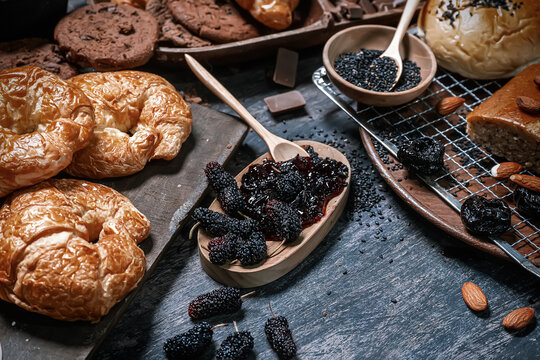 Fresh baked croissants served with mulberry jam and dried prunes on rustic wooden table.