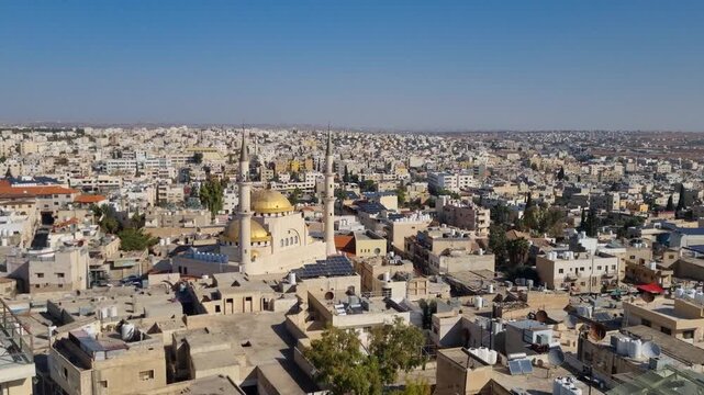 Panoramic skyline view over Madaba, Jordan, with the domes and minaret of King Hussein Mosque shining under the bright midday sun, framed by city rooftops and hills on the horizon