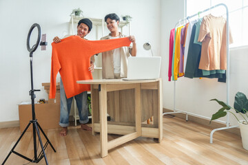 Two Smiling Young Men Enthusiastically Showcase Orange Sweater While Live Streaming