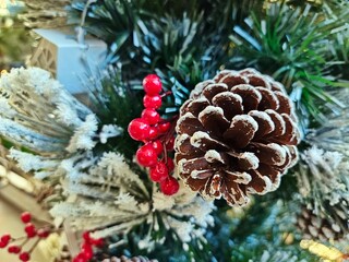 Pine cones, red berries, handmade small white cardboard houses wihte blurred pine tree as background for Christmas decoration.