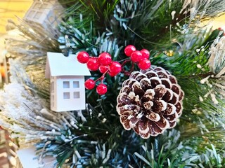 Pine cones, red berries, handmade small white cardboard houses wihte blurred pine tree as background for Christmas decoration.