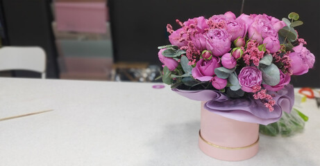 Delicate bouquet of lush pink peony roses and delicate spray flowers, arranged in a soft pink cylindrical box. Accented with eucalyptus leaves, it’s a beautiful gift or decoration.