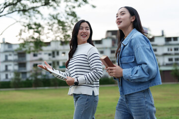Young women students walking talking in park holding books